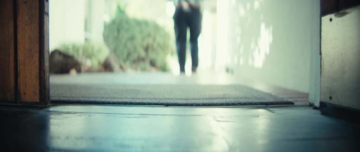The camera captures a groundlevel view of a doorway where a persons feet appear and walk through the entrance the individual continues walking away from the camera and down a brightly lit hallway