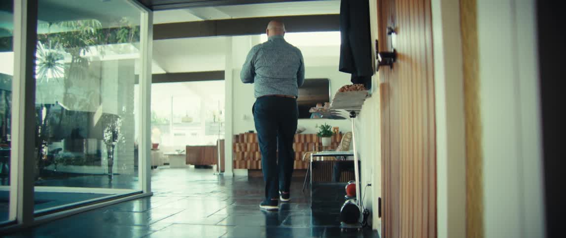 The man enters the home and hangs his jacket up