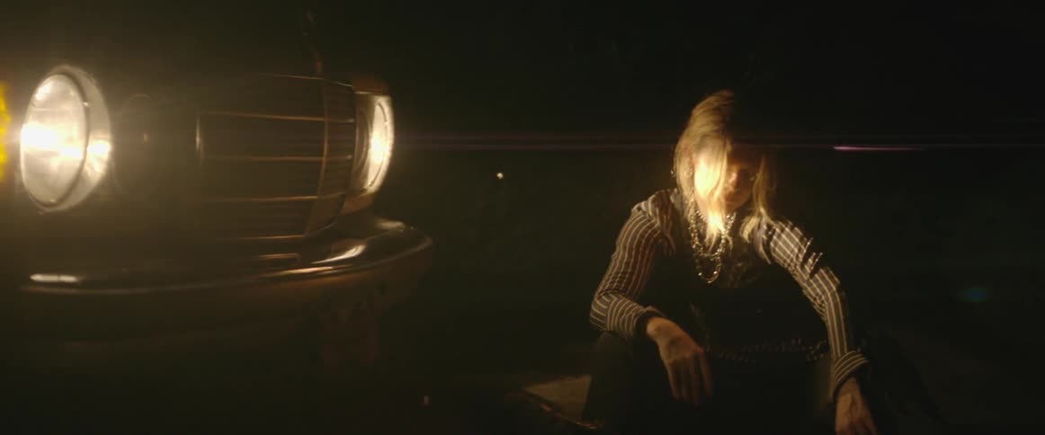 A woman dances in front of car headlights at night