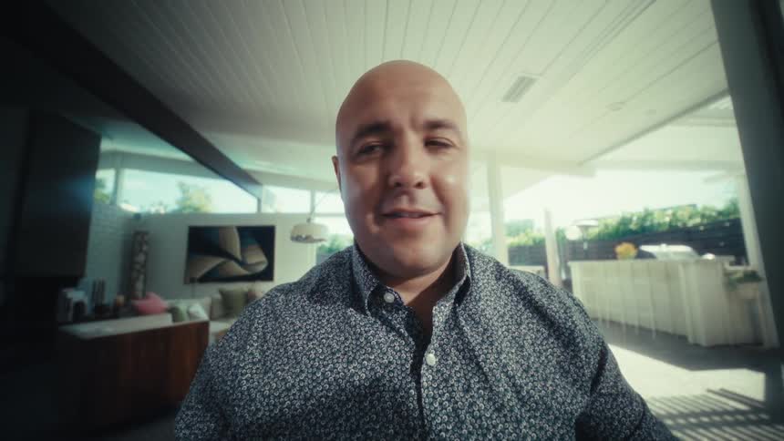 A man with a shaved head sits at a table in a modern sunlit room initially reviewing printed charts and graphshe sets the papers aside and look