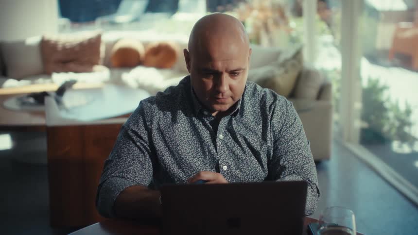 Man seated at a table looks at a laptop with his hands near the keyboard