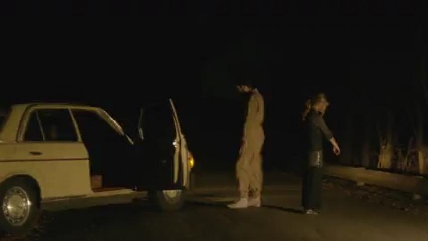A man and woman stand in front of a car with flashing lights