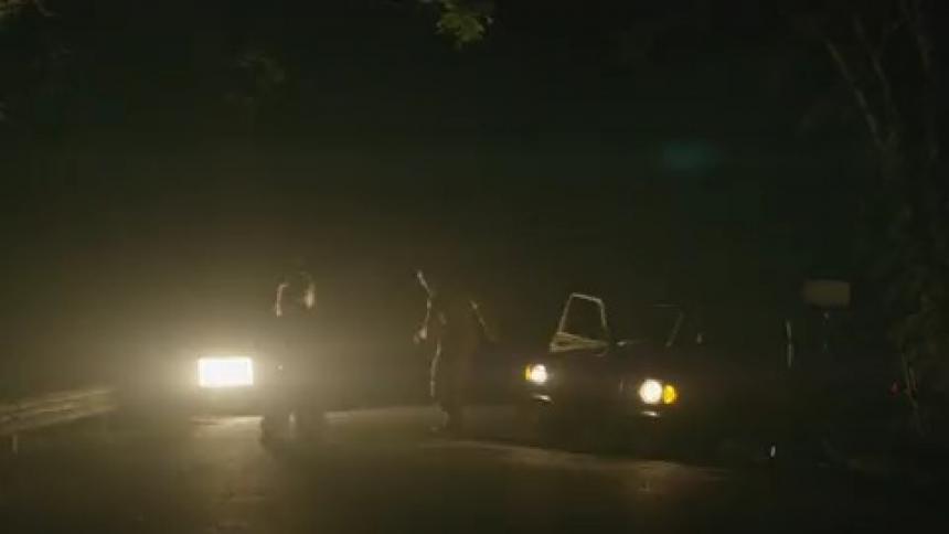 A man and woman dance in front of a car with flashing lights