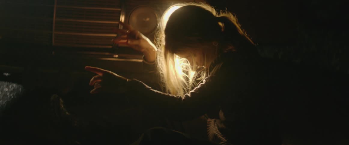 Woman moving rhythmically as she sits outdoors in front of a car with its headlights on at night