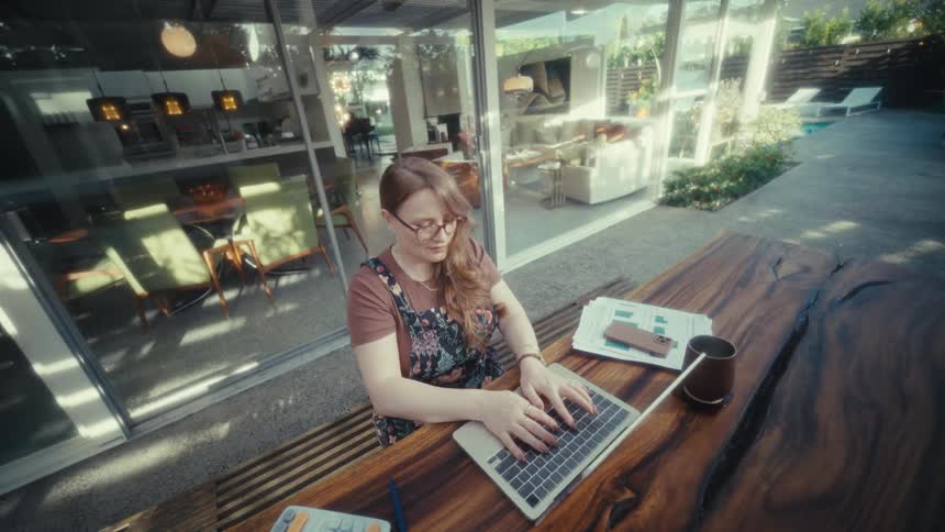 Woman wearing glasses opening stripedcover laptop on outdoor table in front of glass doors