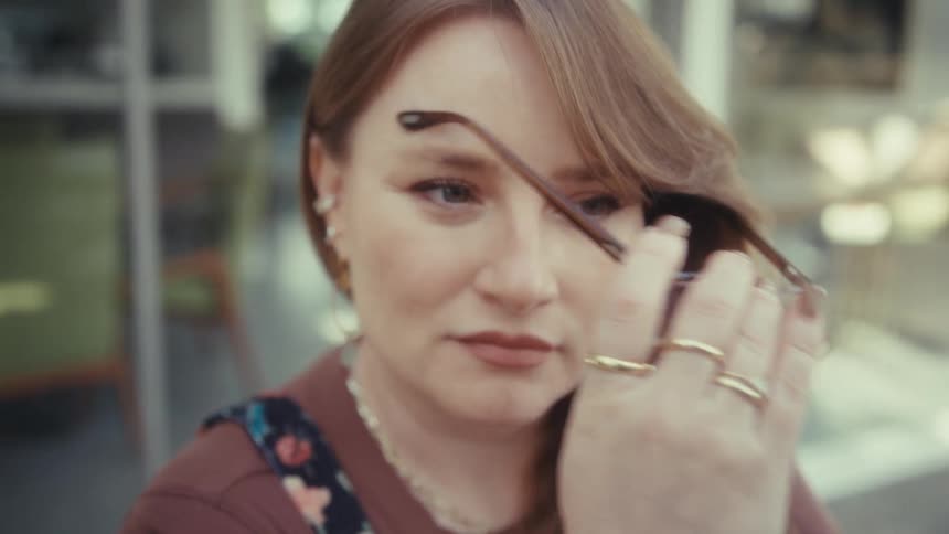 A woman removes her glasses and looks away while sitting outdoors