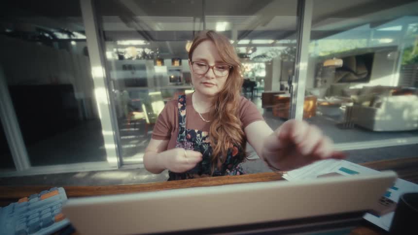 A woman sitting at a desk and opening a laptop that features a distinct design on its outer shell this design consists of several horizontal stripes in different colors