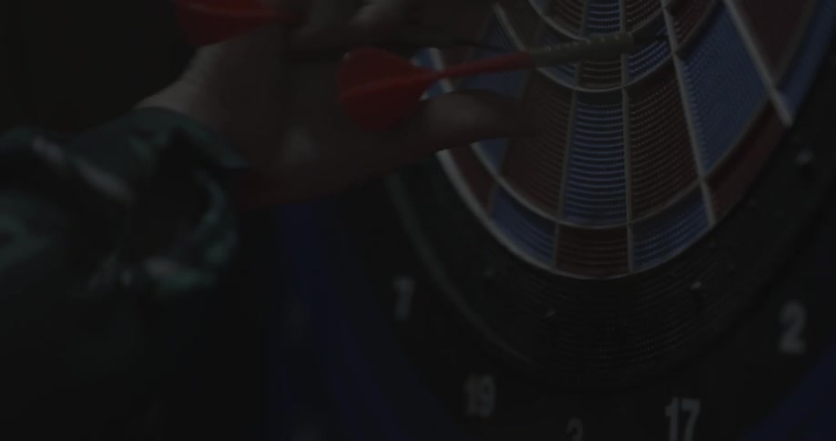 A man removes red darts off of a dartboard