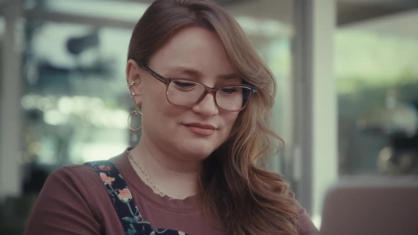 Woman wearing glasses using stripedcover laptop at table in front of glass doors