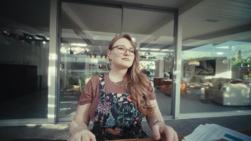 Woman wearing glasses closing stripedcover laptop on table in front of glass doors