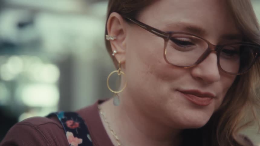 Woman wearing glasses looking downward with focused expression in illuminated setting