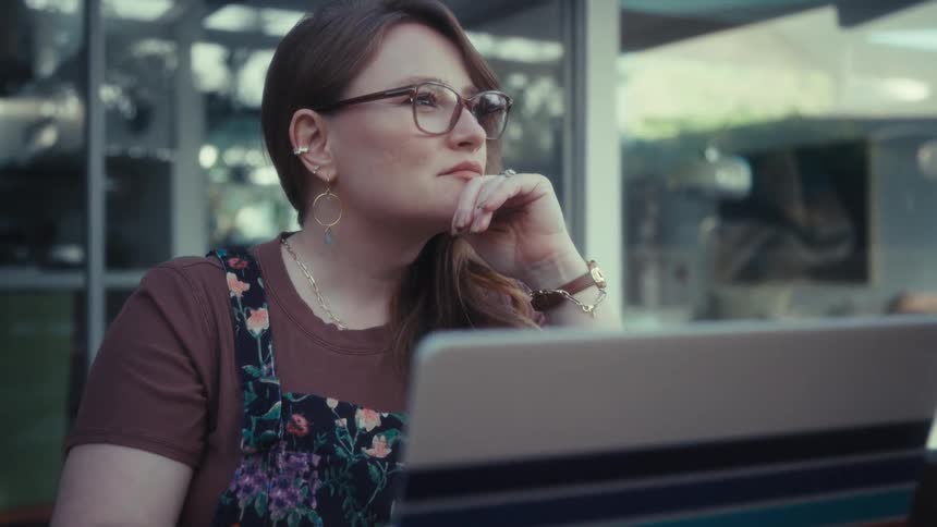 Woman wearing glasses using stripedcover laptop at outdoor table in front of glass doors