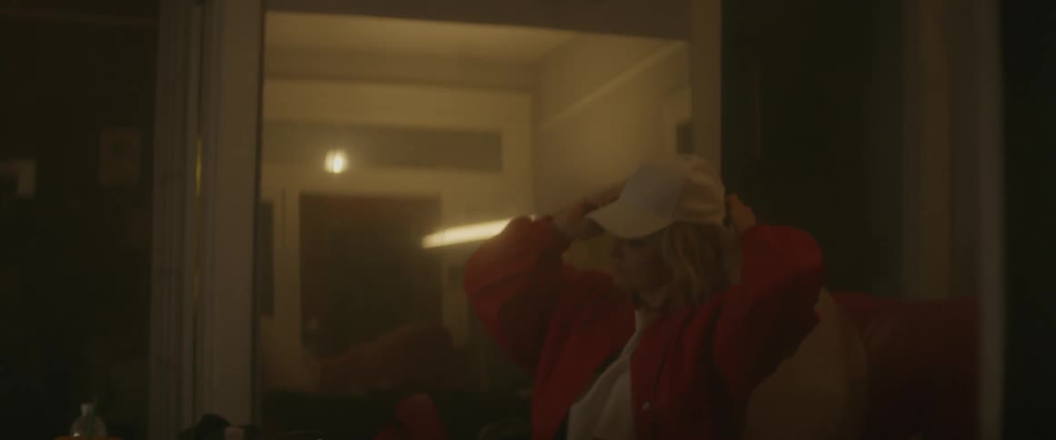Man throwing pages into the air while a blonde woman puts on a baseball cap indoors