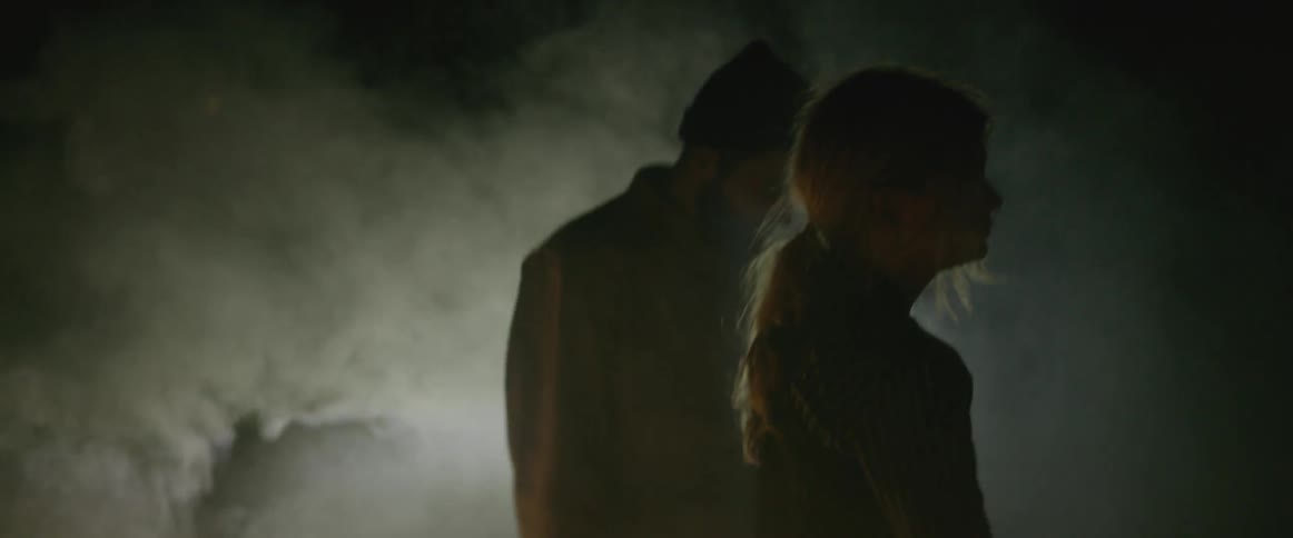 Smoke hovers around a woman and man pacing about outside at night