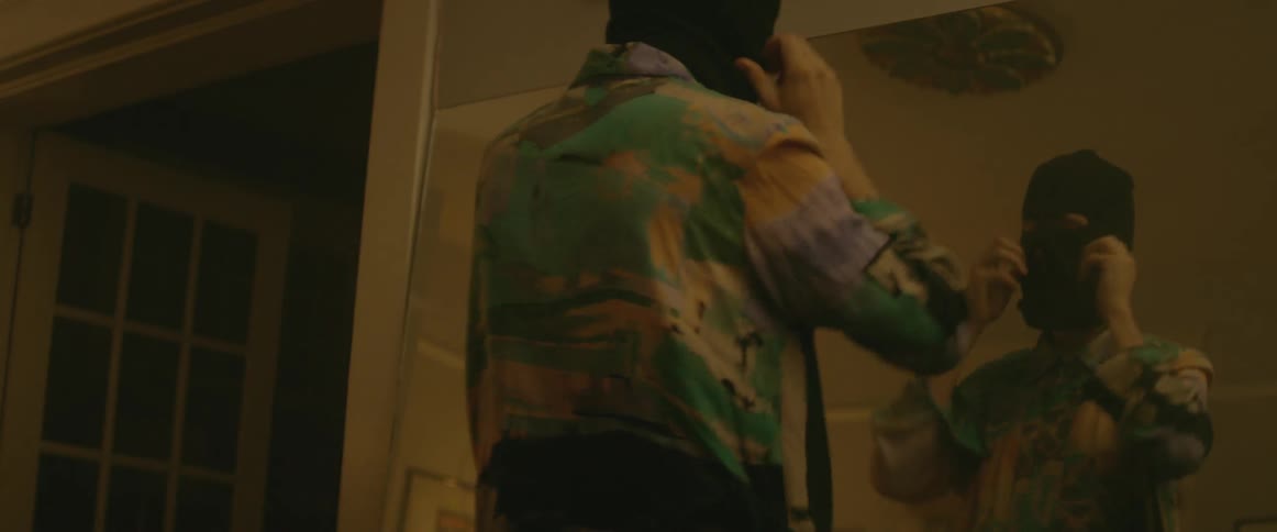 Man putting on a black ski mask in front of a mirror