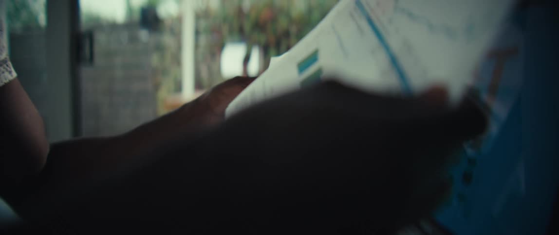 A black man flips through printed documents beside an open laptop displaying charts on the screen