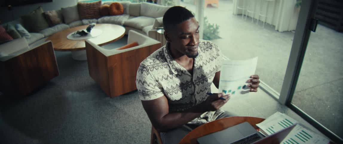 Man sitting at a table having a conversation on a laptop computer and looking at paperwork