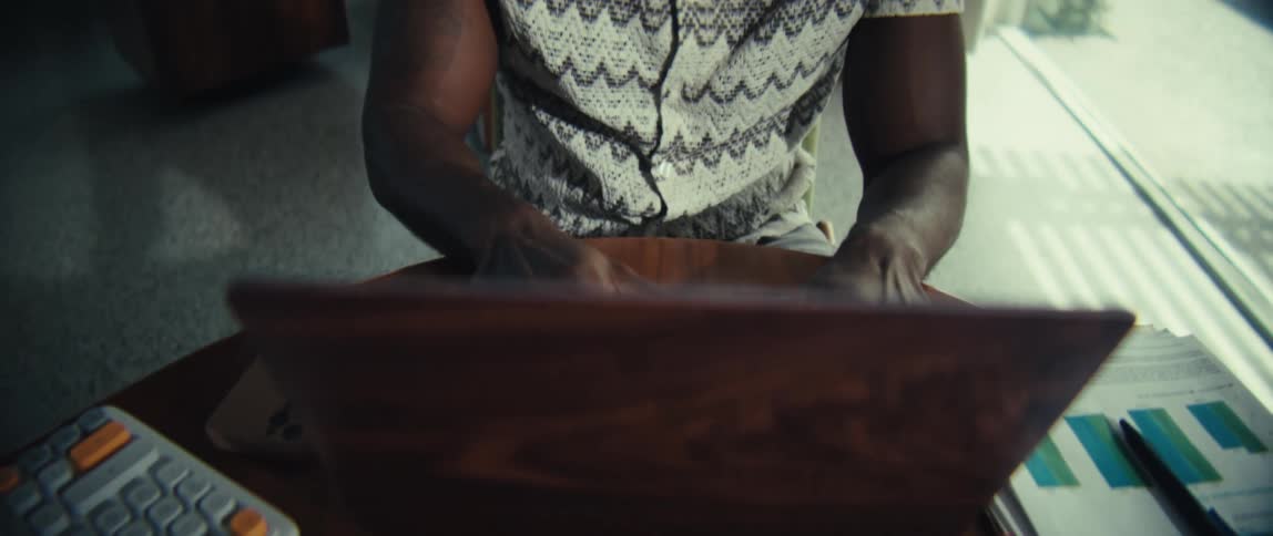 Hands type on a laptop on a desk with a calculator and documents beside it