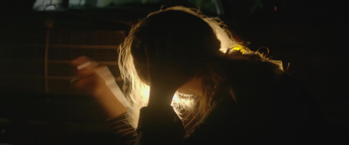A woman dances in front of a car's headlights