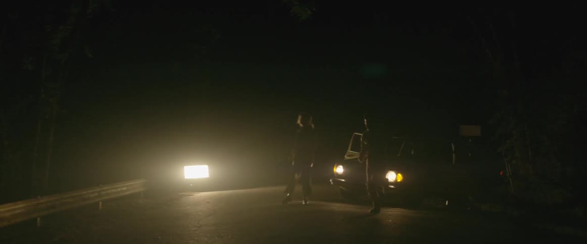A man and woman dance in front of a car with flashing lights