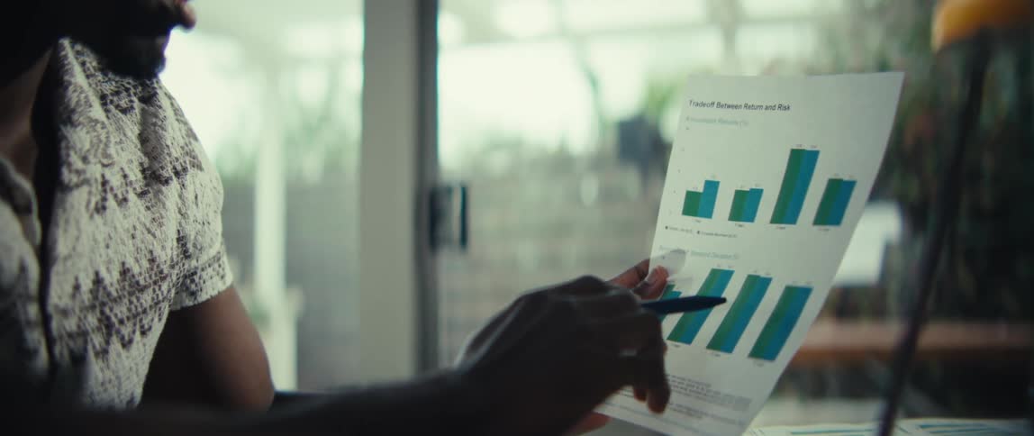 Hand points to a bar chart on a sheet held in front of a laptop