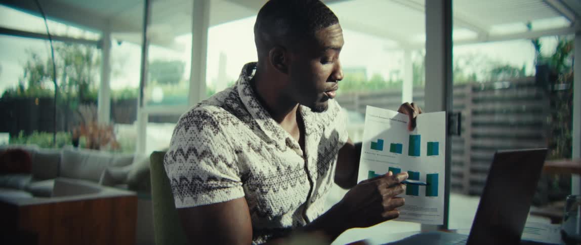 The man is discussing a bar graph with someone on the laptop