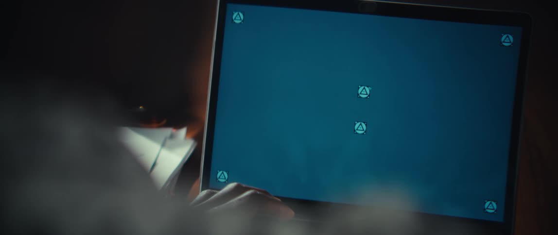 A close view from behind a person showing a laptop with a solid blue screen and tracking markers while a hand uses a white calculator on a wooden table
