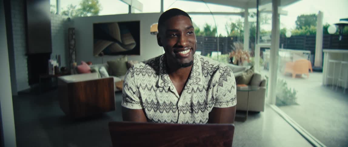 Man sitting at a table typing on a laptop computer and he smiles