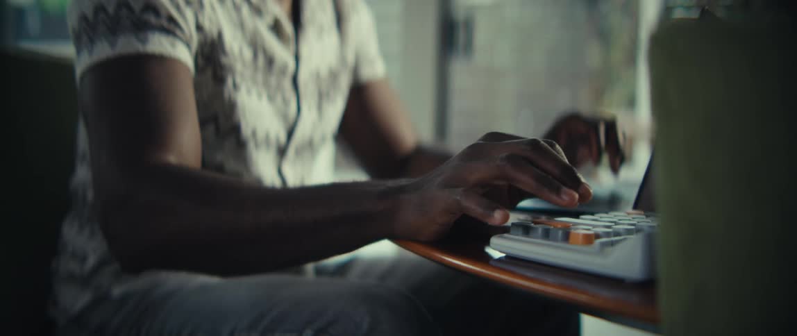 The man is typing on a calculator while looking at a laptop