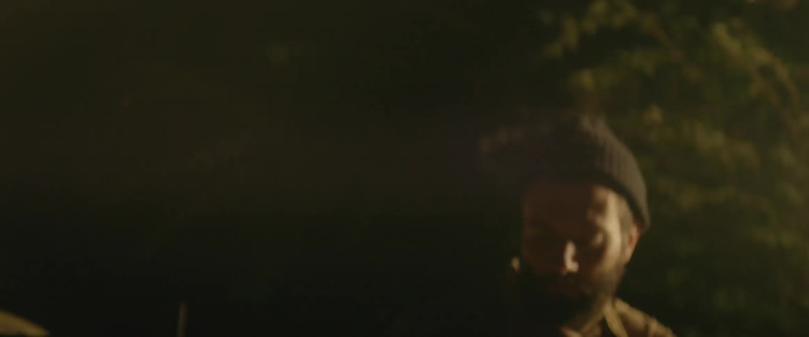 Lights shine on a bearded man getting out of a car