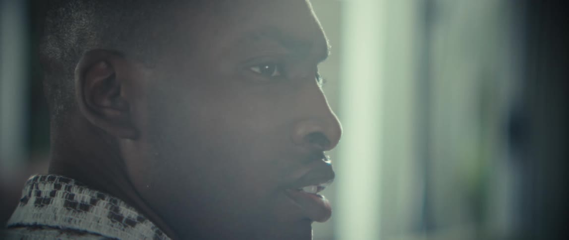A black man is captured in a close up profile view as he speaks indoors