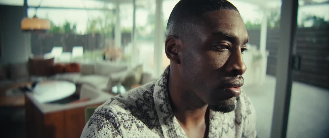 A black man sits at a table in a modern living room reviewing documents and holding a pen while focusing intently on the papers in front of him