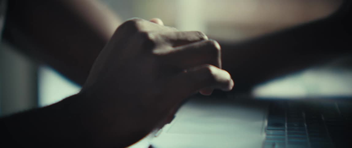A black man is scrolling on a laptop in deep thought in a sunlit room