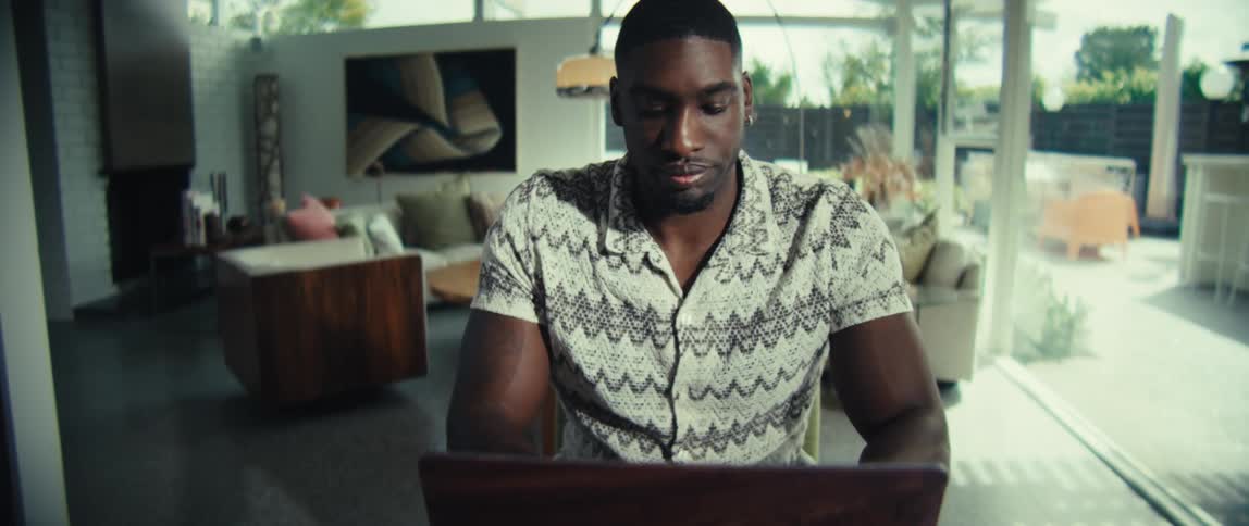 A young black man sits in front of a computer typing at midday