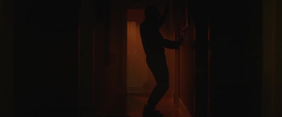 A man dances in a dark hallway while lights flash