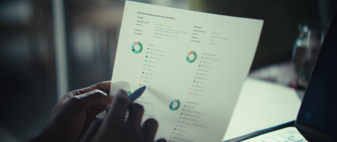 Person holding document with circular charts and laptop in background