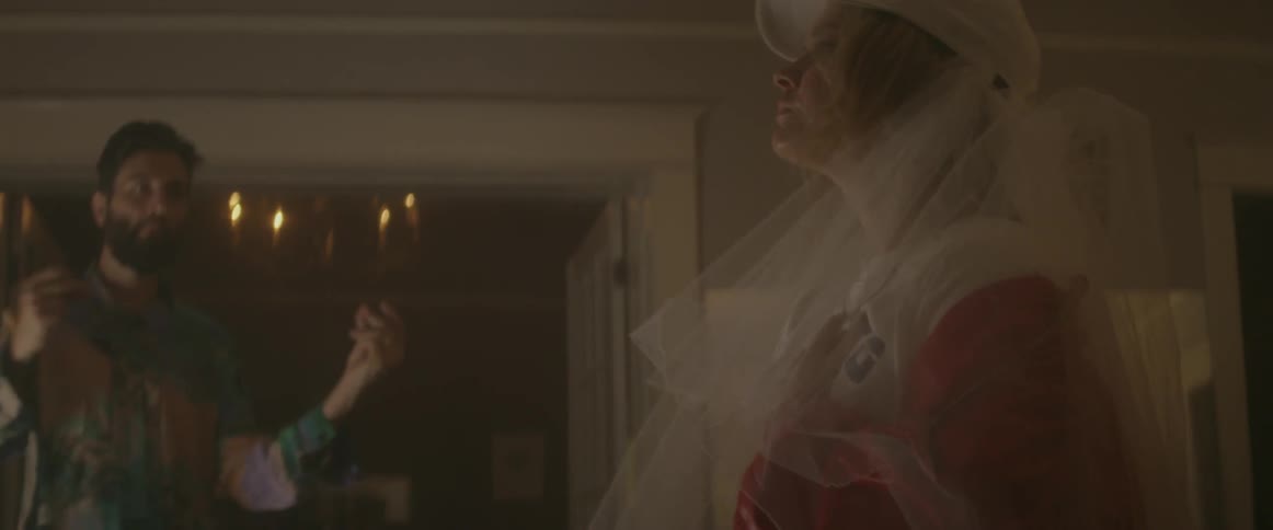 Woman dancing indoors wearing a white baseball cap with a veil beneath it and a man dancing next to her