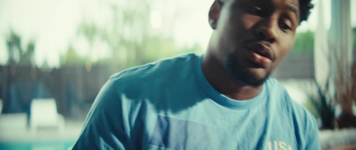A black man is sitting in a sunlit room using a game controller