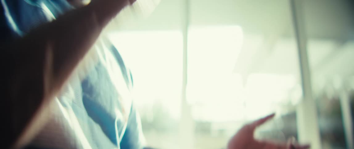 A young man sits outdoors clapping excitedly as sunlight streams through a nearby window