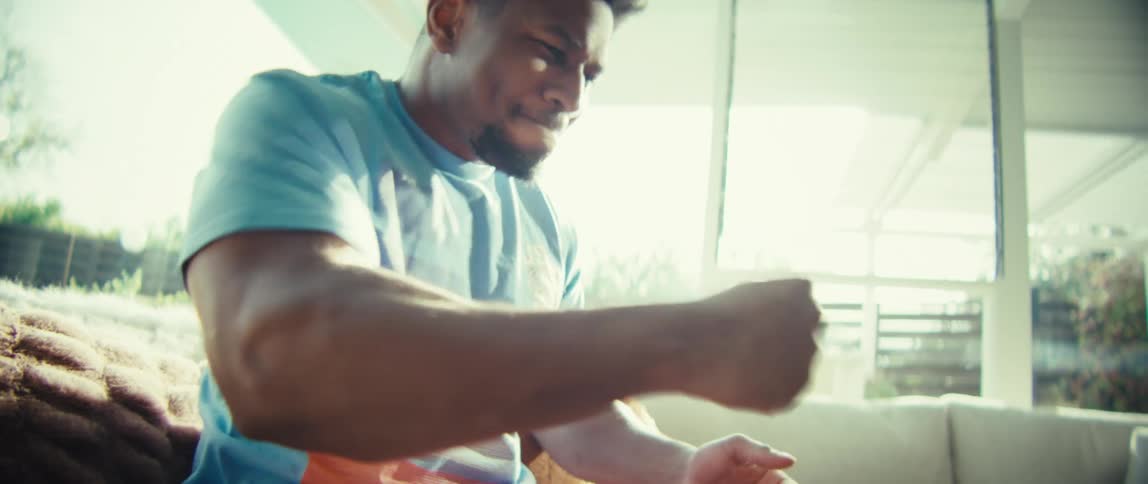 A young man sits on a couch while intently focused on a tablet screen in front of himhis expressions shift from deep concentration to a brief cheerful smile as he interacts with the device