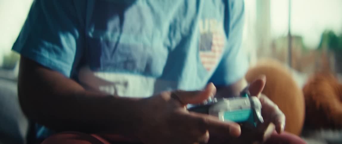 A black man sits happily smiling and cheering as he looks forward using a game controller in a sunlit room