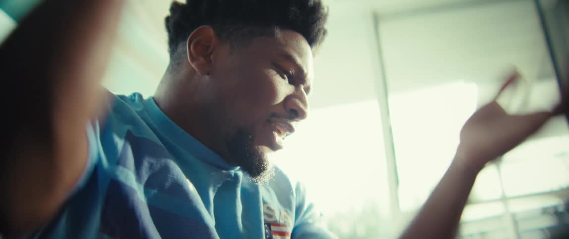 A young man sits watching a game cheering and clapping excitedly as sunlight streams into the room through the glass window