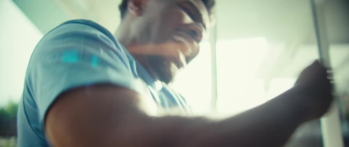 A young man sits indoors clapping and cheering excitedly as sunlight streams through the window