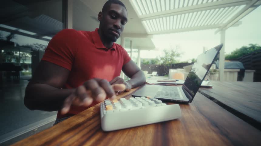 A man sitting at a table on an outdoor patio uses a calculator and laptop