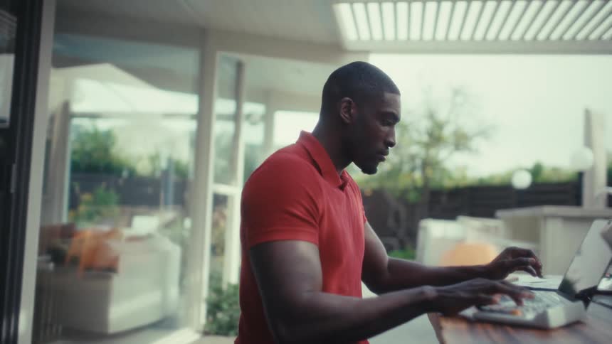 Man sitting in front of a computer on the patio uses a calculator