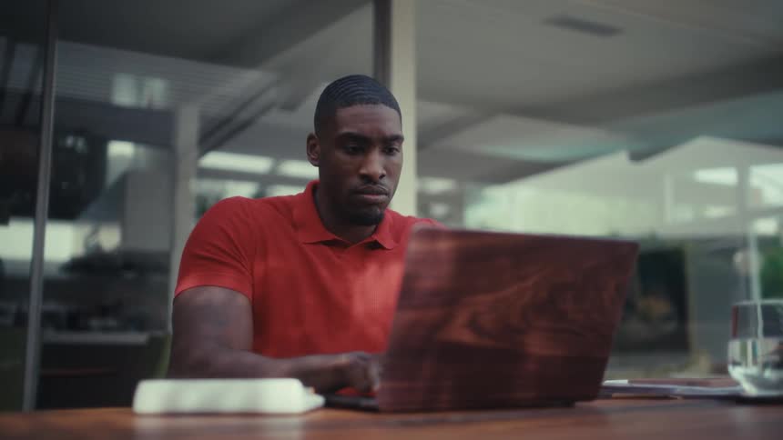 Man seated at a table uses a laptop while touching a calculator beside it