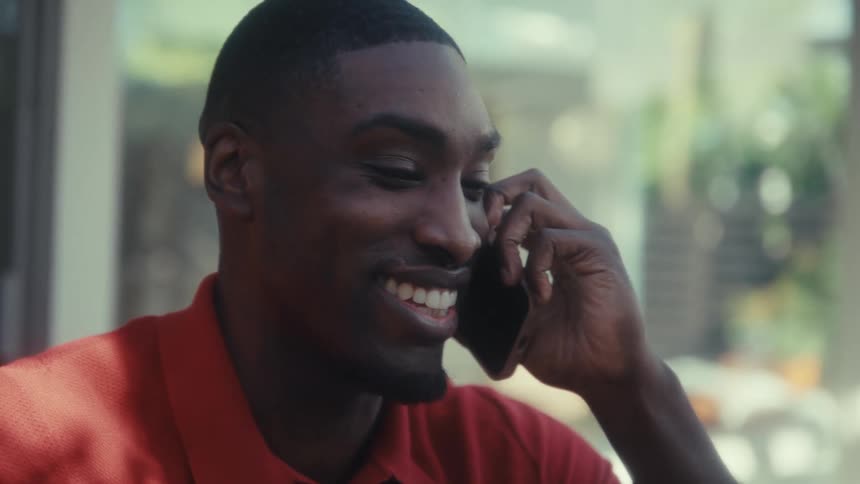 Man talking on the phone laughs before hanging up and clasping his hands together while smiling