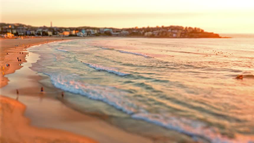 People have a great time on the beach at sunset with a city skyline in the background as waves crash along the shoreline