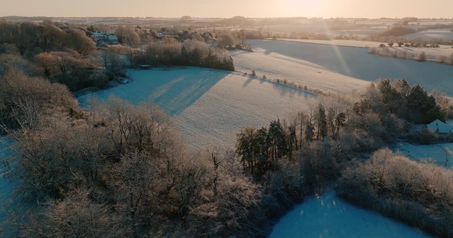 Sunlight shines upon a snow covered field surrounded by forests