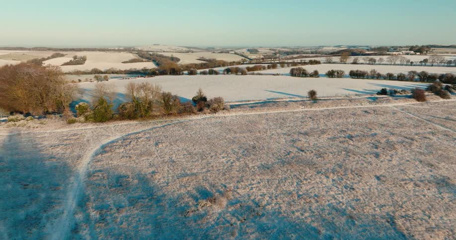 Field covered in snow with sparse vegetation and roads outdoors during dusk or dawn